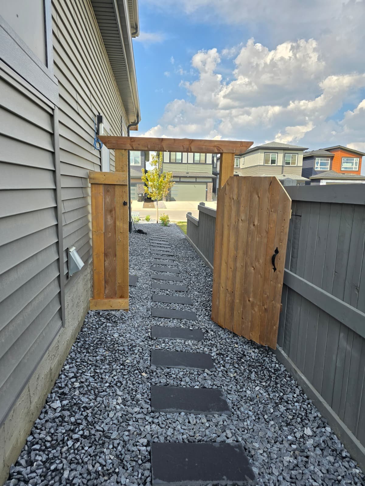 Dark stone stepper path through cedar pergola gate — Edmonton